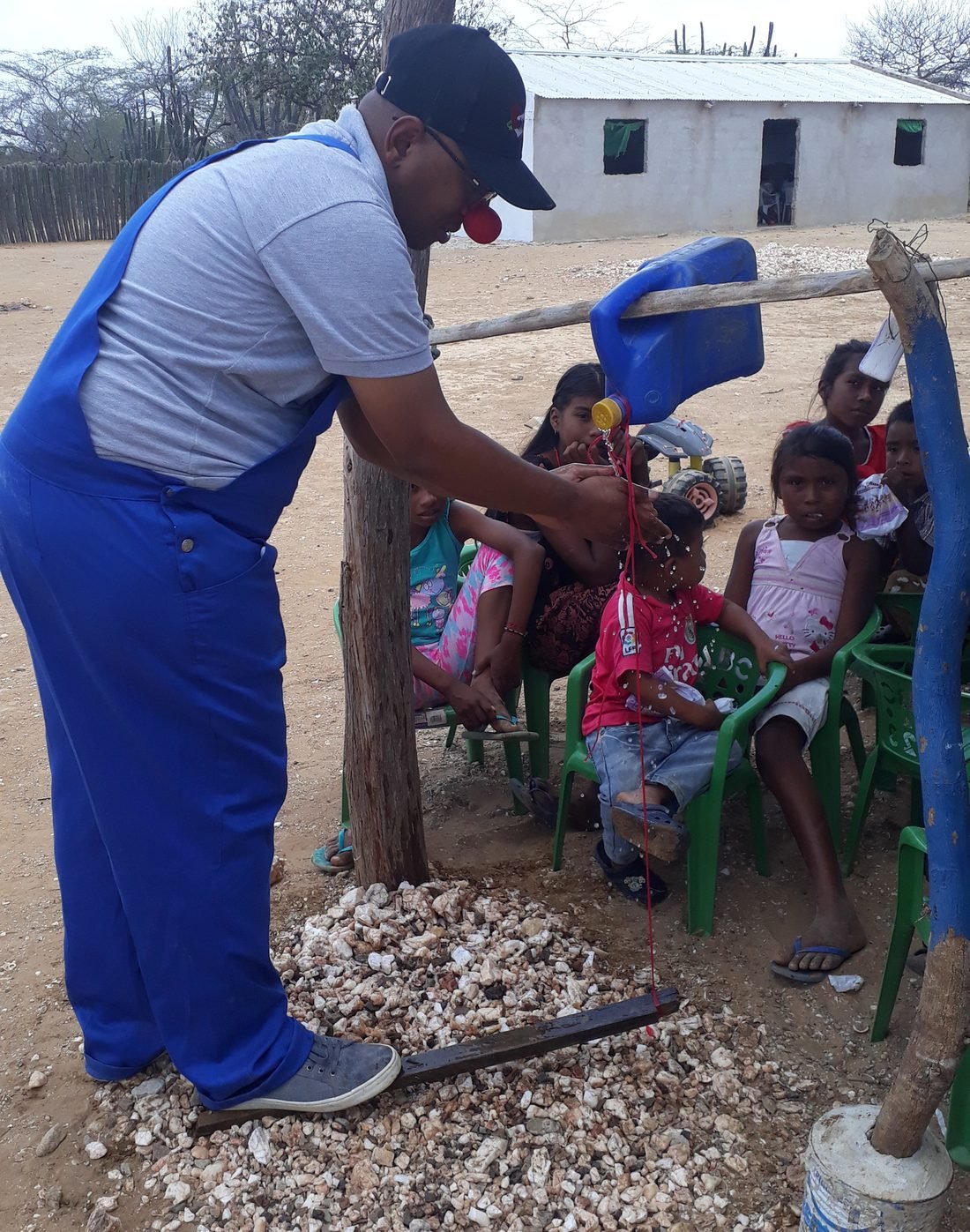 Voluntario reparte agua a un grupo de niños sentados bajo la enramada
