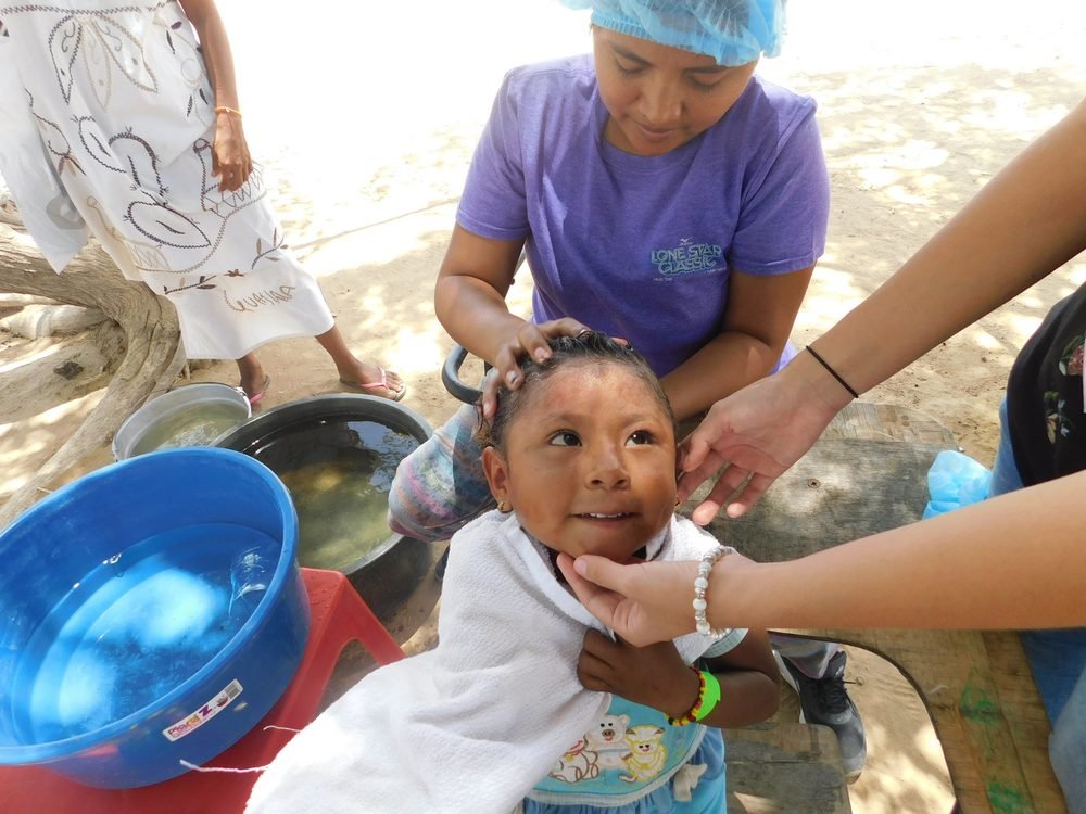 Voluntaria revisando el cabello de una niña wayúu durante una jornada de higiene