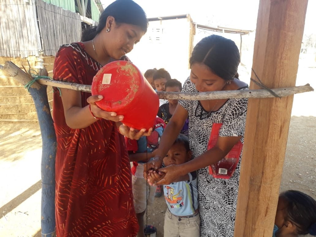 Dos voluntarias ayudan a un niño a lavarse las manos en un taller de higiene en la ranchería